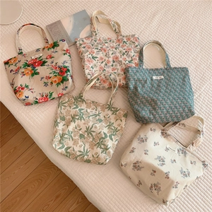 Detail showing five floral cotton tote bags with simple wish labels on a textured fabric
