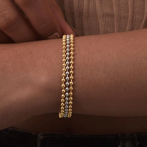 Close-up of triple-layered gold and silver stainless steel beaded bracelets on wrist
