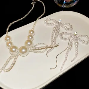 Elegant silver bow pearl necklace and earring set displayed on a white ceramic dish