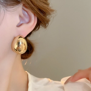 Gros plan d'un modèle portant une boucle d'oreille goutte dorée au fini poli brillant