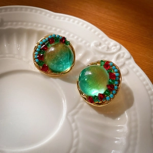Détail de boucles d'oreilles vintage en or avec résine verte et perles sur assiette blanche