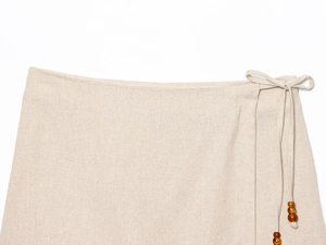 Détail de jupe en lin beige avec cordon de taille et perles décoratives en bois brun