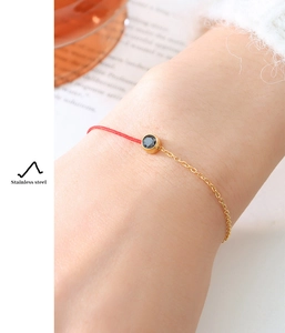 Detail of red cord and gold stainless steel chain bracelet with a black gemstone charm