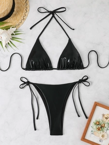 Detail of glossy black metallic bikini set with tie-side bottom on marble background