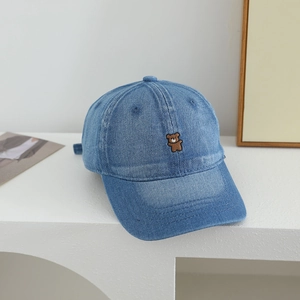 Close-up of blue denim baseball cap featuring detailed bear embroidery on white stand