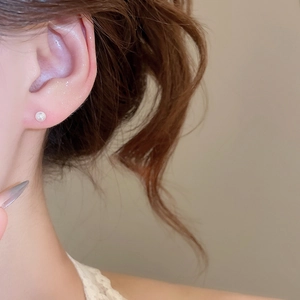 Macro shot of a white round pearl stud earring worn on a model's ear with soft lighting