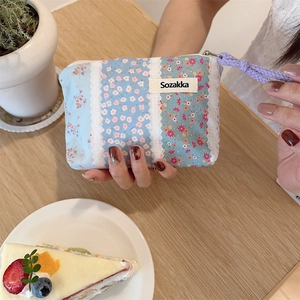 Close-up of small floral fabric pouch with zipper and purple cord in hand