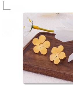 Detailed macro view of gold five-petal flower earrings with a matte brushed metal finish