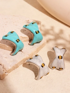 Detail of C-shaped enamel earrings in lake blue and pearly white with gold glitter