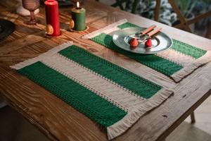 Detail of woven table mat with dark green stripes and boho tassels on wooden table