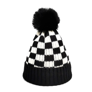 Close-up of checkerboard knit beanie with a large faux fur pom-pom detail