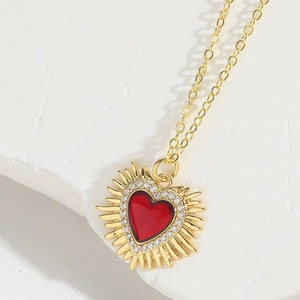 Detail of a sunburst gold necklace featuring a ruby red heart stone and micro-pave zircons