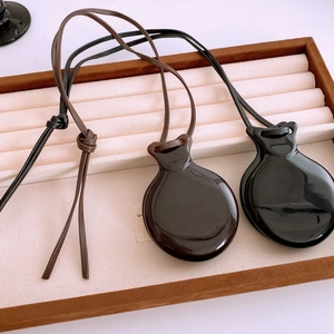 Close-up of minimalist deep brown and black mirror-finish pendants on fine leather cords