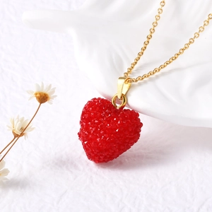 Gros plan du pendentif cœur rouge sur chaîne dorée avec décor en céramique blanche