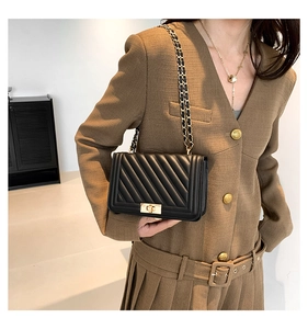 Detail of a black quilted patent leather bag with gold chain strap and turn-lock closure