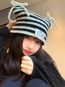 Detailed close-up of knit texture with devil ears and white bow on striped beanie