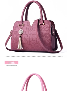 Detail of pink crocodile embossed handbag featuring golden V-shaped buckle and fringe charm