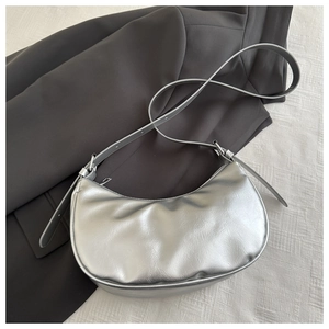 Silver crescent underarm bag displayed on gray blazer with adjustable strap detail