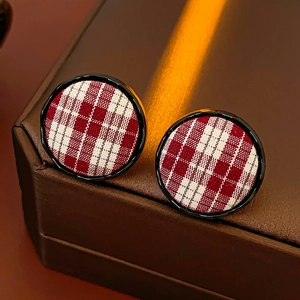 Macro shot of red and white plaid fabric button earrings with glossy black edges on leather
