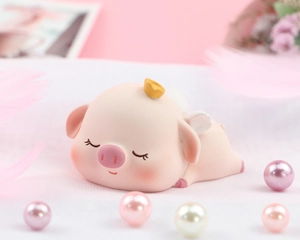 Close-up of sleeping pink pig figurine with golden crown and white wings on feather