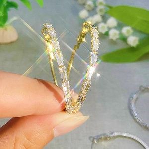 Luxurious gold hoop earrings with sparkling rectangular zircons shown in a hand-held view