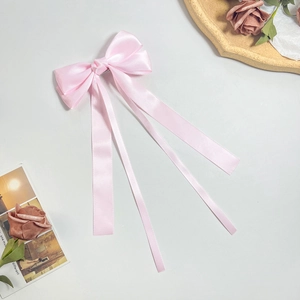 Elegant pink satin bow hair clip with long ribbons on a vintage aesthetic background