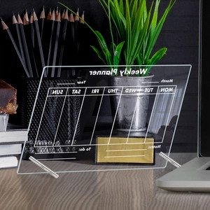 Close-up of a clear acrylic weekly planner board on a desk with metal stands