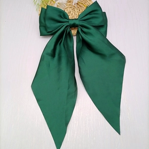 Close-up of deep green satin bow hair clip with elegant long ribbons on wooden surface