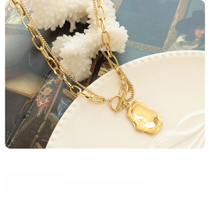 Detailed view of layered gold necklace with irregular pendant on a ceramic dish