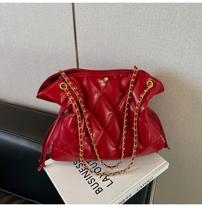 Detail of red quilted leather bucket bag with gold chain strap on a business magazine