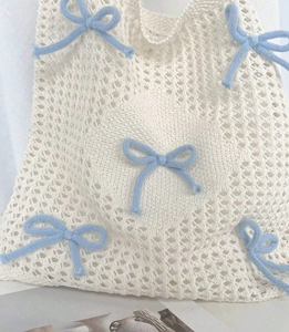 Close-up of white knitted tote bag with light blue bows and intricate openwork texture