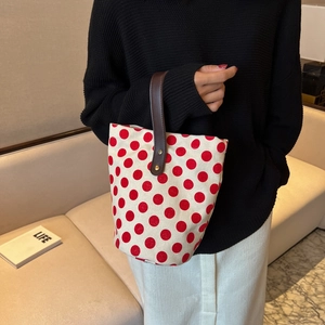 Minimalist polka dot canvas bucket bag with brown leather handles held by a model