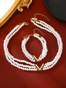 Détail du parure de perles à trois rangs avec accent doré en V sur soie rouge