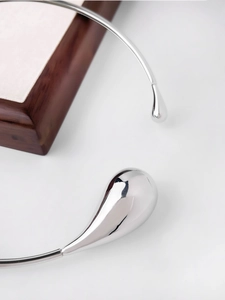 Detailed close-up of polished silver waterdrop open necklace with asymmetric metal design