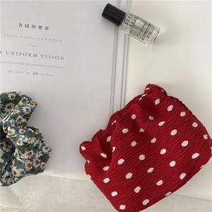 Flat lay of red polka dot and green daisy floral scrunchies on a textured fabric surface