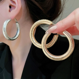Close-up of large textured gold and silver hoop earrings with sparkling metallic finish