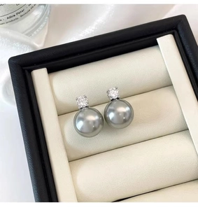 Macro shot of grey pearl earrings with sparkling zircon inlay on black leather stand