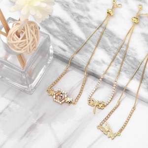 Adjustable gold bracelets with dragonfly and butterfly zircon charms on marble surface