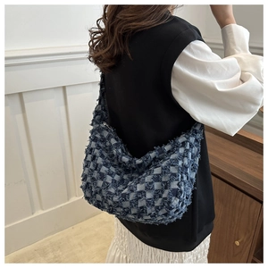 Detail of blue denim crossbody bag with checkerboard pattern and frayed fringe edges