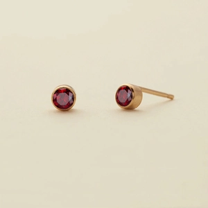 Close-up of minimalist gold plated stud earrings featuring round red gemstones