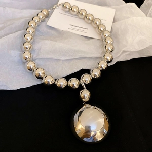Macro shot of silver chunky bead necklace with large mirror sphere pendant on white paper