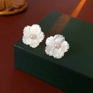 Vue macro de boucles d'oreilles fleur en nacre et perle sur une boîte cadeau de luxe
