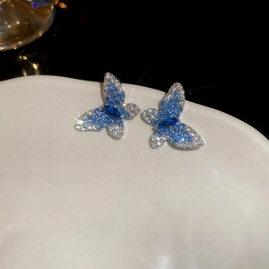 Close-up of blue gemstone butterfly earrings with silver diamonds on white plate