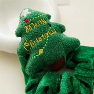 Close-up of green plush Christmas tree scrunchie with yellow Merry Christmas embroidery