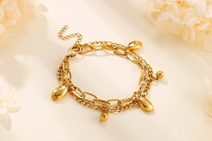 Detail eines goldenen zweischichtigen Kettenarmbands mit ovalen Anhängern auf beigem Grund