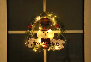 Detail eines beleuchteten Weihnachts-Schneemann-Kranzes mit Tannennadeln und Beeren