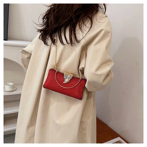 Red glitter evening clutch bag with gold leaf clasp and chain strap on a trench coat