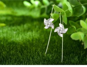 Macro shot of silver windmill drop earrings hanging on a green leaf with soft natural light