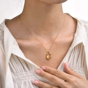 Close-up of a gold irregular hollow pendant necklace worn by a model in a white shirt