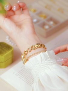 Detail of layered gold bracelets with heart and pearl charms worn on wrist with a white cuff